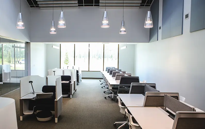 Desks line sides of room with high ceilings and big windows